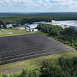Aerial view of large solar panel farm adjacent to industrial manufacturing facilities surrounded by forest