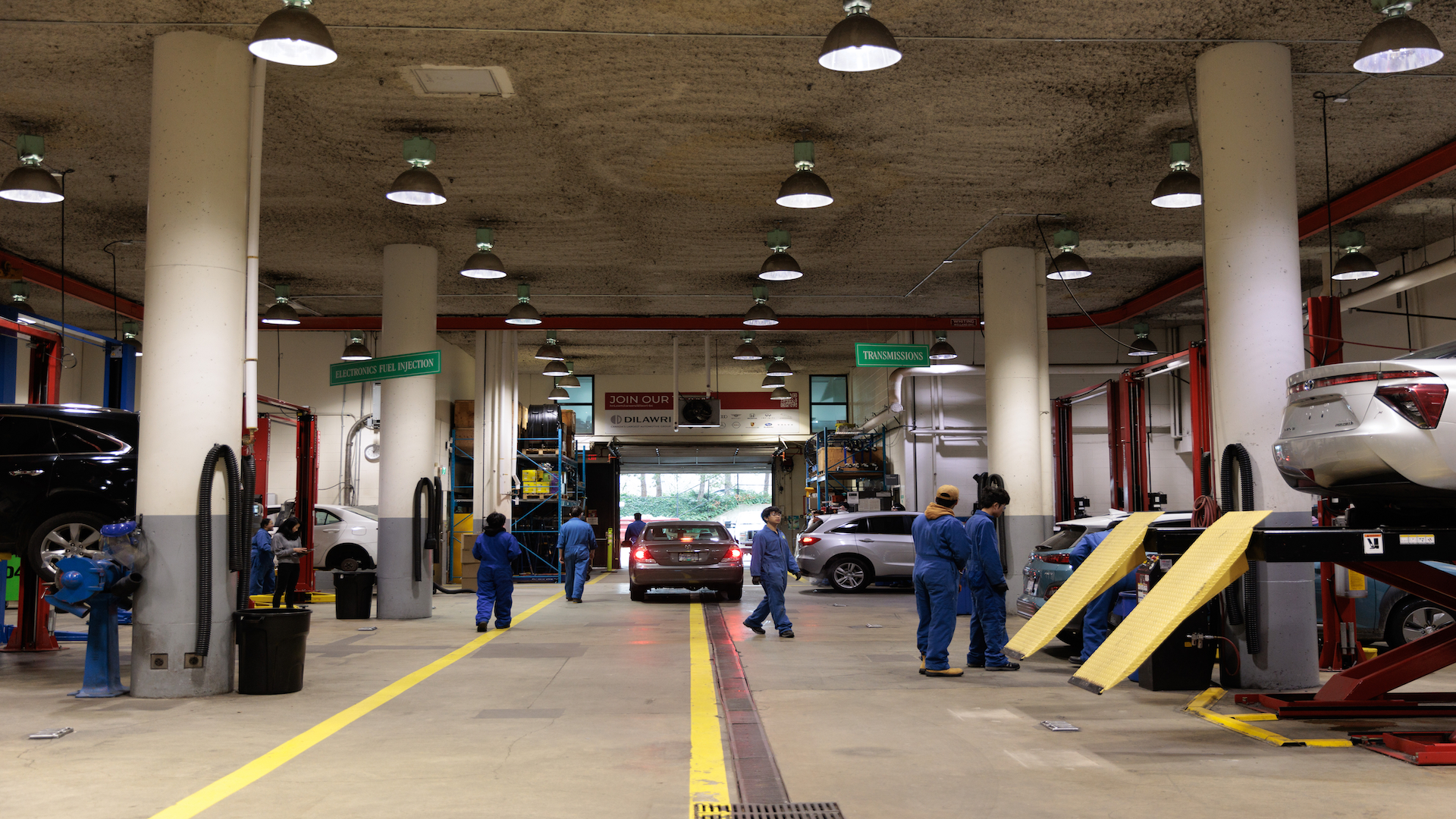 Professional automotive service garage with technicians in blue uniforms working on vehicles under bright overhead lighting