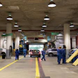 Professional automotive service garage with technicians in blue uniforms working on vehicles under bright overhead lighting