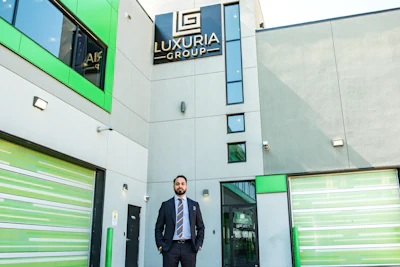 Professional man in business suit standing in modern office building lobby with Luxuria Group signage and green accent walls