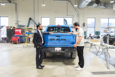 Salesman and technician inspect blue RAM pickup truck in automotive service facility