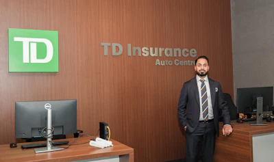 Professional man in business suit standing in TD Insurance Auto Centre office with TD Bank logo on green wall