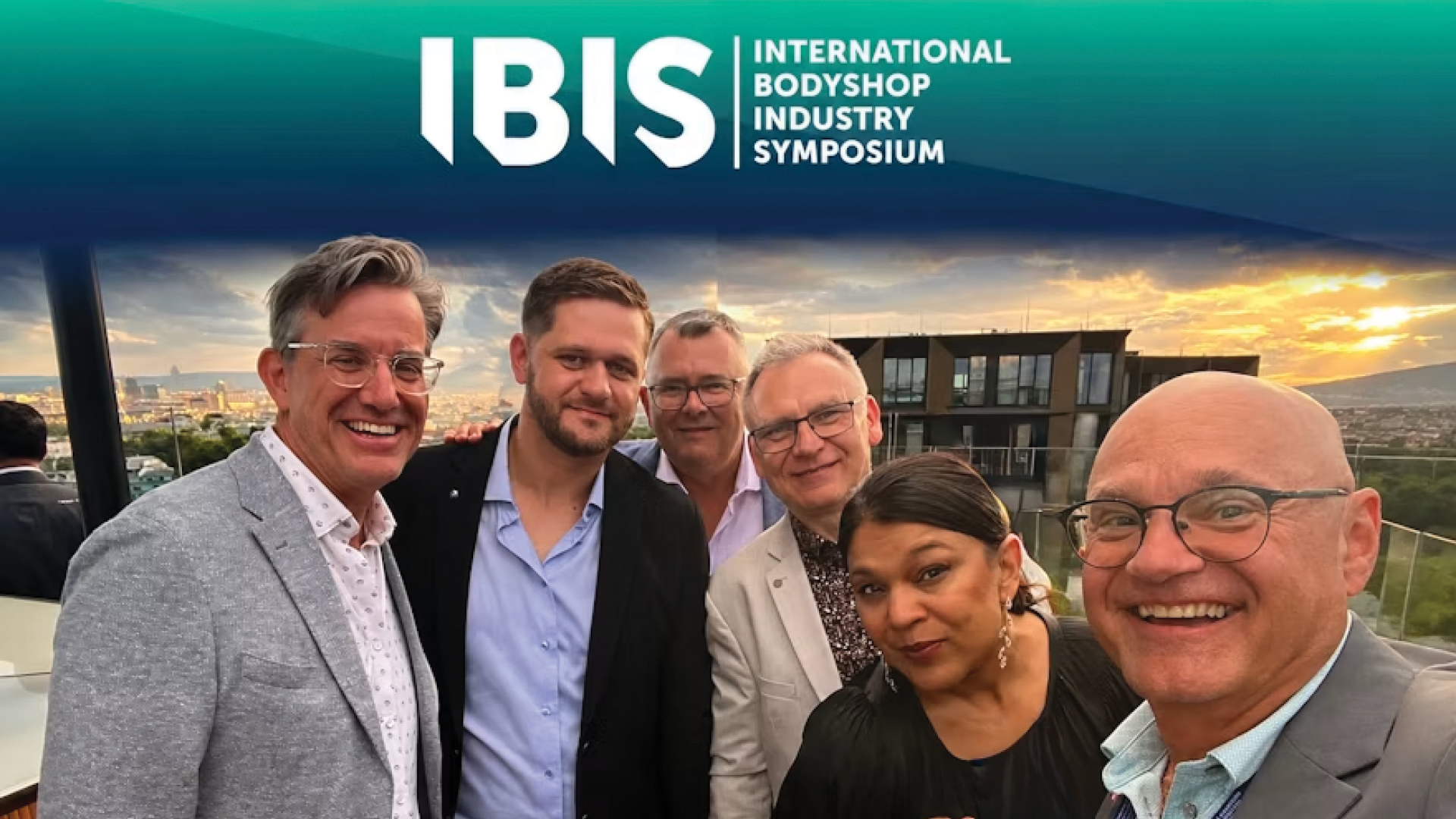 Six professionals posing together at sunset during the International Bodyshop Industry Symposium event
