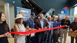 Group of professionals at ribbon-cutting ceremony with red ribbon and APT signage in background