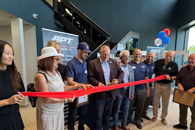 Group of professionals at ribbon-cutting ceremony with red ribbon and APT signage in background