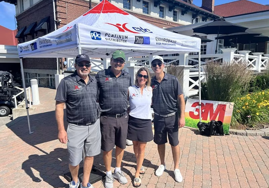 Four team members in branded apparel stand together at a 3M and Platinum Automotive promotional tent during an outdoor event.