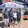 Four team members in branded apparel stand together at a 3M and Platinum Automotive promotional tent during an outdoor event.