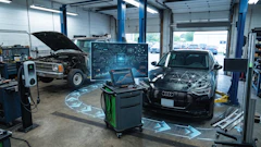 Modern auto repair shop with diagnostic equipment, laptop workstation, and vehicles undergoing service in bright facility