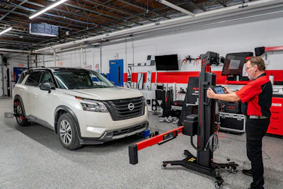 Technician performing vehicle diagnostics on white Nissan SUV in modern automotive service facility