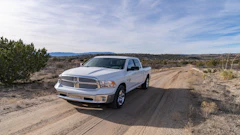 White Dodge Ram pickup truck parked on a dirt road in a desert landscape with mountains in the distance