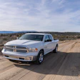 White Dodge Ram pickup truck parked on a dirt road in a desert landscape with mountains in the distance