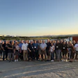 Large group of professionals standing together on a rooftop during sunset with mountains visible in the background