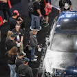 Crowd of spectators gathered around a dark sedan at an automotive event or car show