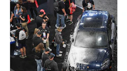 Crowd of spectators gathered around a dark sedan at an automotive event or car show