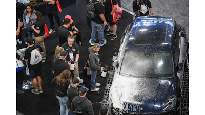 Crowd of spectators gathered around a dark sedan at an automotive event or car show