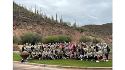 Large group of people posing together on grass with desert hillside and saguaro cacti in background