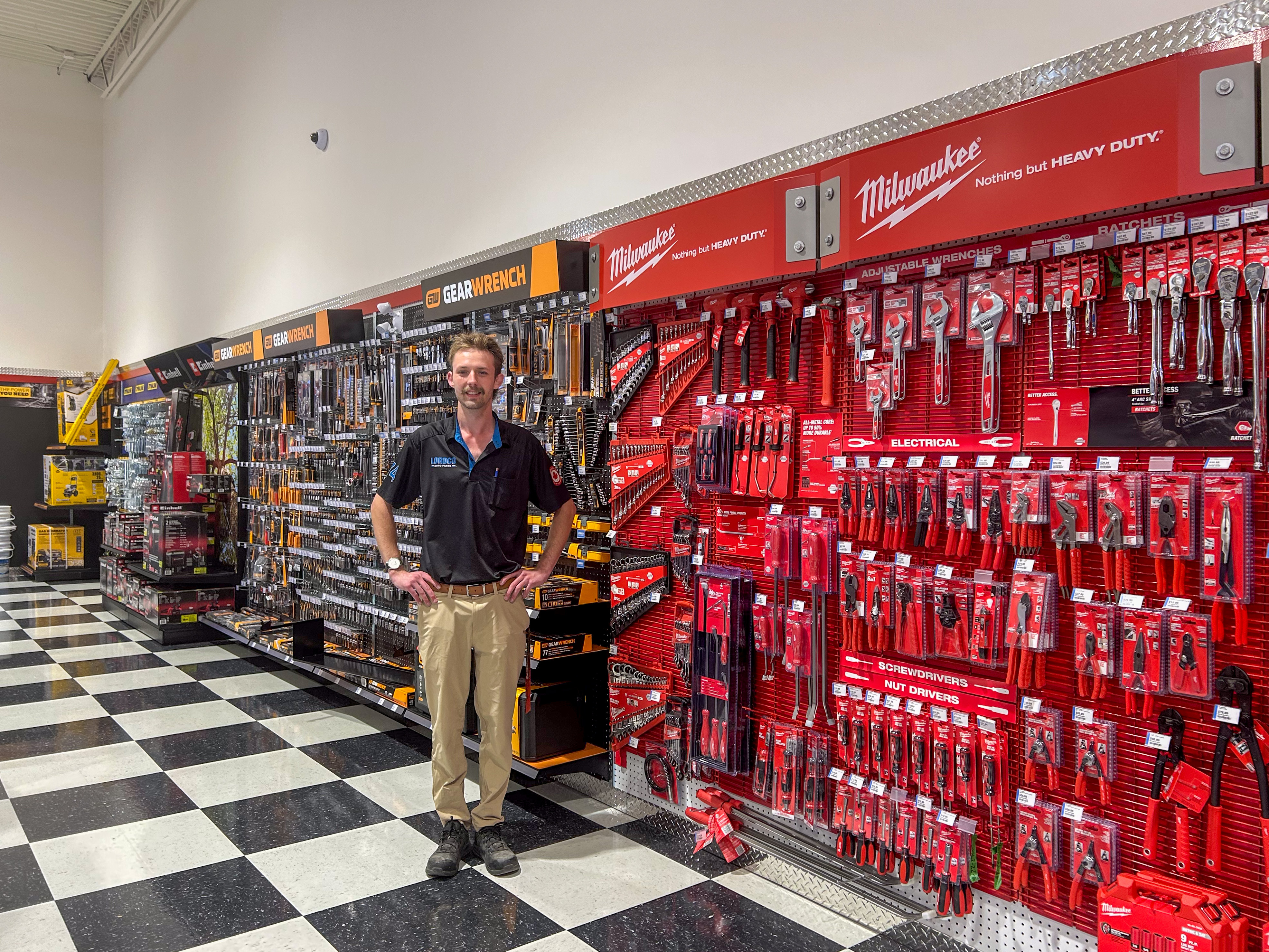 Man standing in tool store showroom with red Milwaukee tool display wall and black and yellow DeWalt pegboard tool organization system.