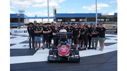 Team of engineers and staff posing with red and black formula racing car at industrial facility