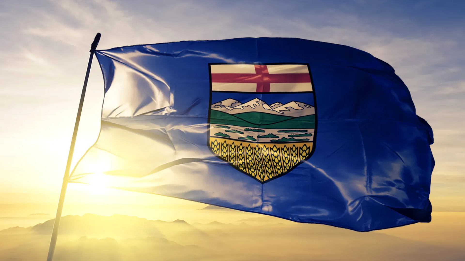 Alberta provincial flag waving at sunset with coat of arms emblem featuring mountains and wheat