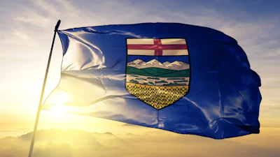 Alberta provincial flag waving at sunset with coat of arms emblem featuring mountains and wheat