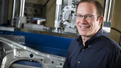 Professional man wearing glasses and navy shirt smiling in front of industrial manufacturing equipment