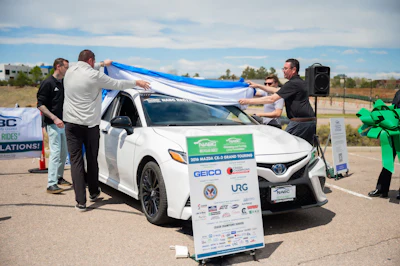 Team members unveiling blue ribbon on white Toyota at outdoor charity or promotional event