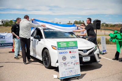 Team members unveiling blue ribbon on white Toyota at outdoor charity or promotional event
