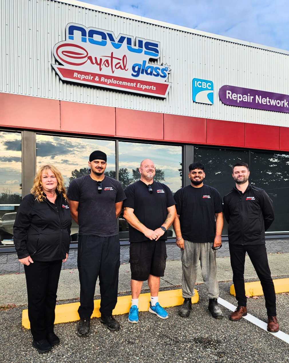 Five team members in black uniforms stand outside Nevus Weld Glass repair shop storefront
