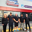 Five team members in black uniforms stand outside Nevus Weld Glass repair shop storefront