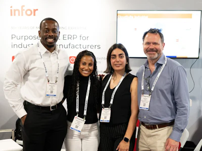 Four professionals wearing conference badges pose together at an Infor business event with presentation materials visible in the background.