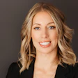 Professional headshot of a woman with shoulder-length blonde hair smiling against a gray background