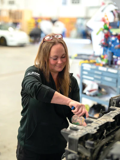Woman working on engine assembly in automotive workshop with tools and machinery visible