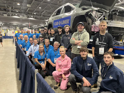 Team of automotive professionals posing in front of damaged vehicle and equipment at industrial facility