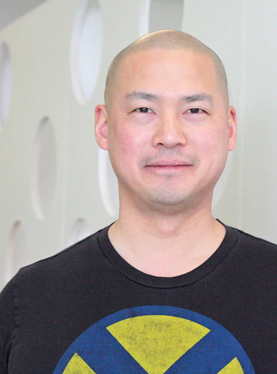 Man with short hair wearing black t-shirt with blue and yellow circular graphic design against neutral background