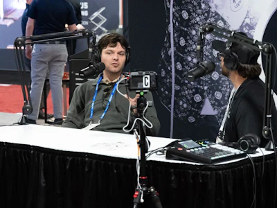 Podcaster speaking into microphone at convention panel with professional broadcasting equipment and audience