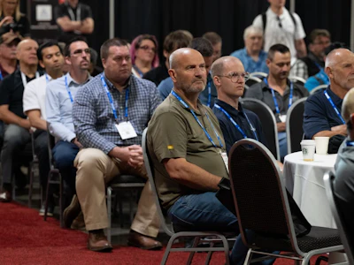Audience members wearing blue ID badges seated at a conference or event venue