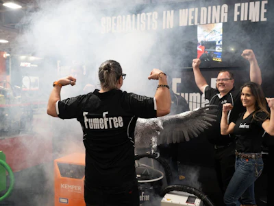 Team celebrates at welding competition event with smoke effects and branded apparel