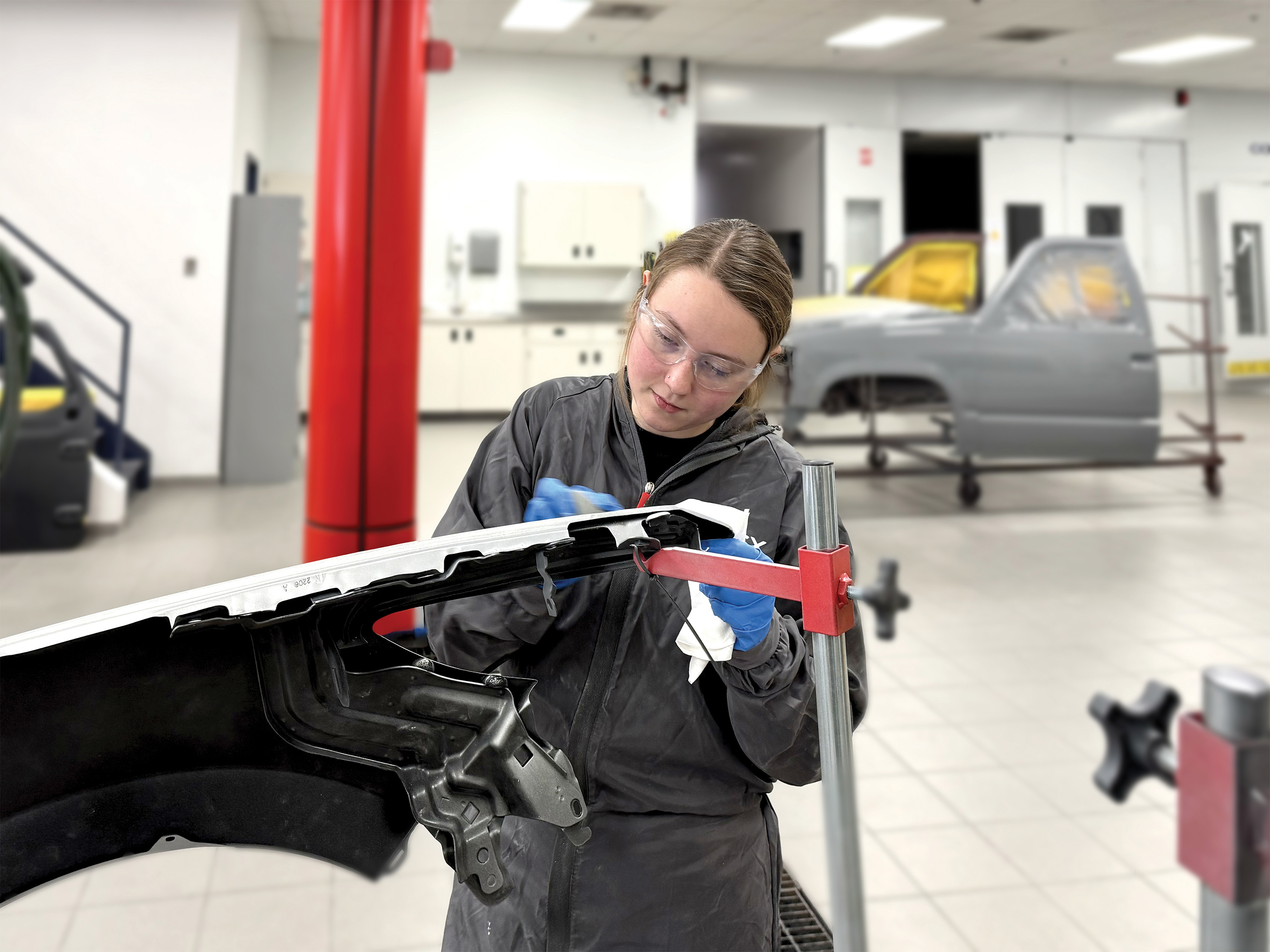 Technician in black jacket inspecting vehicle hood with red tool in automotive repair facility