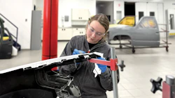 Technician in black jacket inspecting vehicle hood with red tool in automotive repair facility