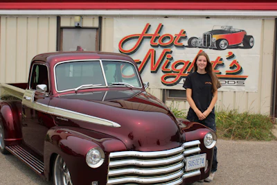 Woman posing beside burgundy vintage hot rod truck at Hot Night's Rods shop