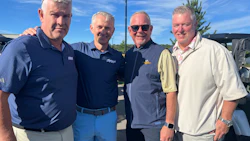 Four men smiling at a golf event on a sunny day with clear blue sky