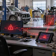 Automotive repair shop workspace with warning alert displayed on desktop monitor and diagnostic tablet