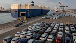 Large cargo ship docked at port terminal with rows of vehicles prepared for export loading.