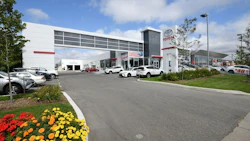 Toyota dealership exterior with white building, parked vehicles, and colorful flower landscaping