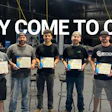Group of eight people holding certificates in an industrial garage setting with text 'Why Come to OKC?'