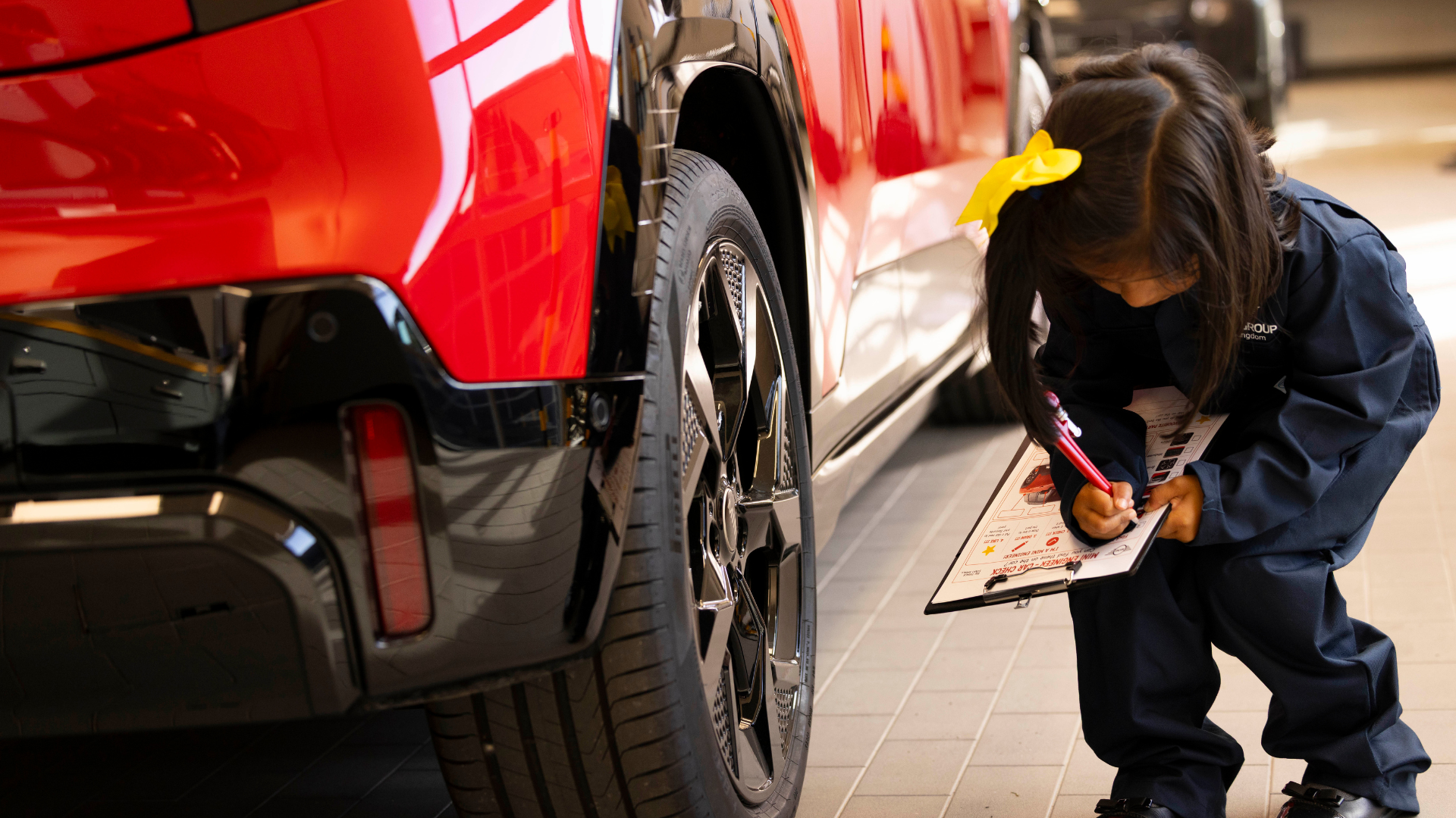 Technician inspecting red vehicle with clipboard in automotive showroom
