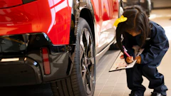 Technician inspecting red vehicle with clipboard in automotive showroom