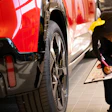 Technician inspecting red vehicle with clipboard in automotive showroom