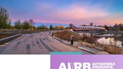 Waterfront park at sunset with curved paving patterns, trees, and red architectural building reflected in water