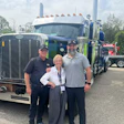 Three professionals posing together in front of blue and green commercial trucks at a trucking industry event